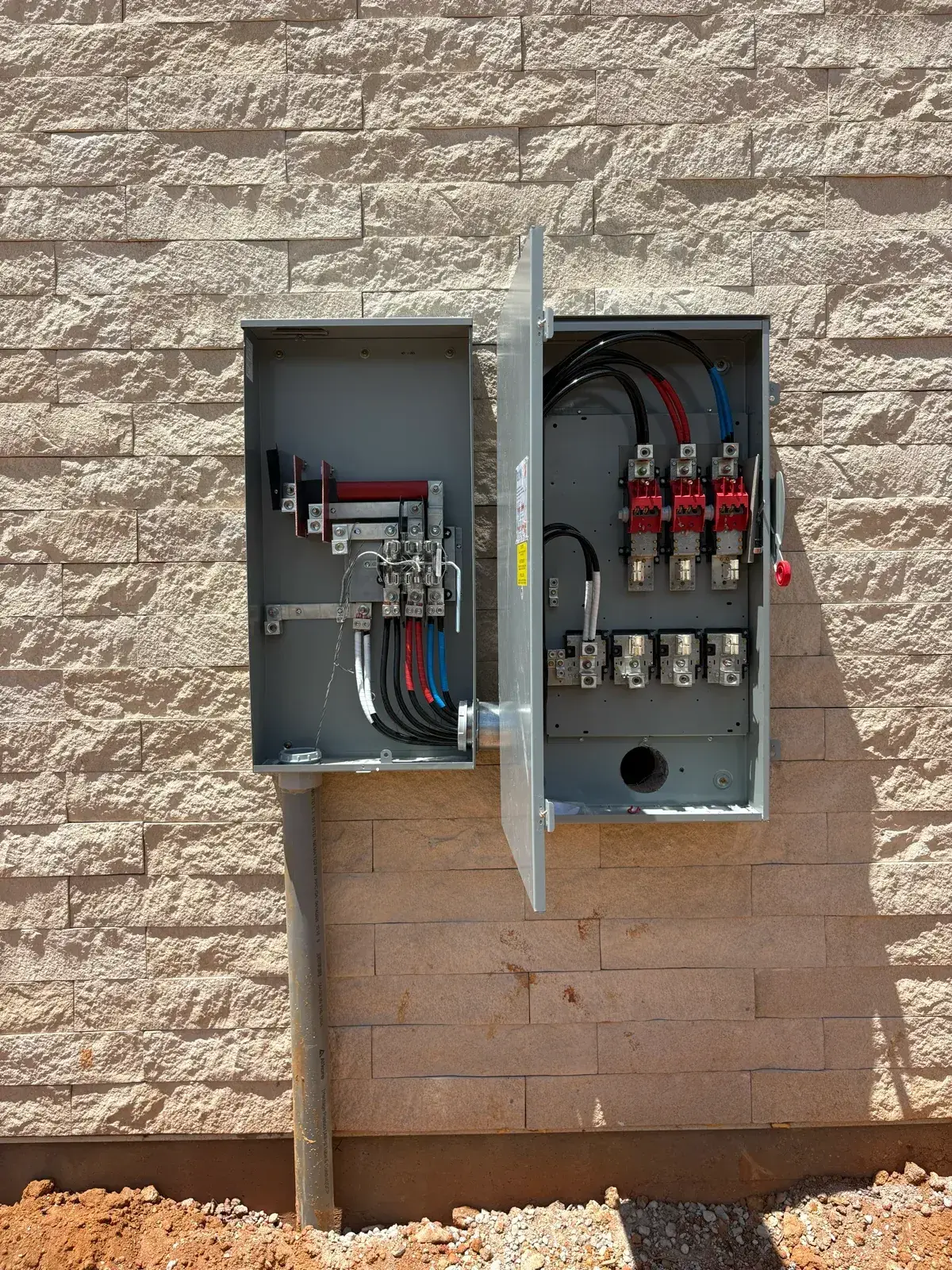 New multi-position meter bank and service disconnect with doors open mid-install, mounted on a split-face block wall at a commercial new-construction site in Baldwin County